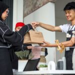 Seorang penjual di kasir sedang melayani pelanggan dengan memberikan produk yang dibeli, mencerminkan peluang usaha modal kecil yang menjanjikan di tahun 2025